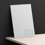 Elegant paper mockup leaning against a dark wall on a wooden shelf, with minimalistic numbering for presentation and design display.