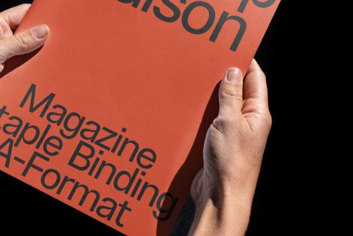 Person holding a red magazine mockup with sample text, displaying staple binding and A-format size, ideal for graphic design templates.