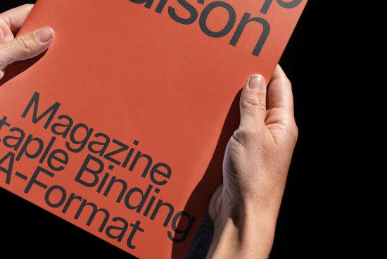 Person holding a red magazine mockup with sample text, displaying staple binding and A-format size, ideal for graphic design templates.