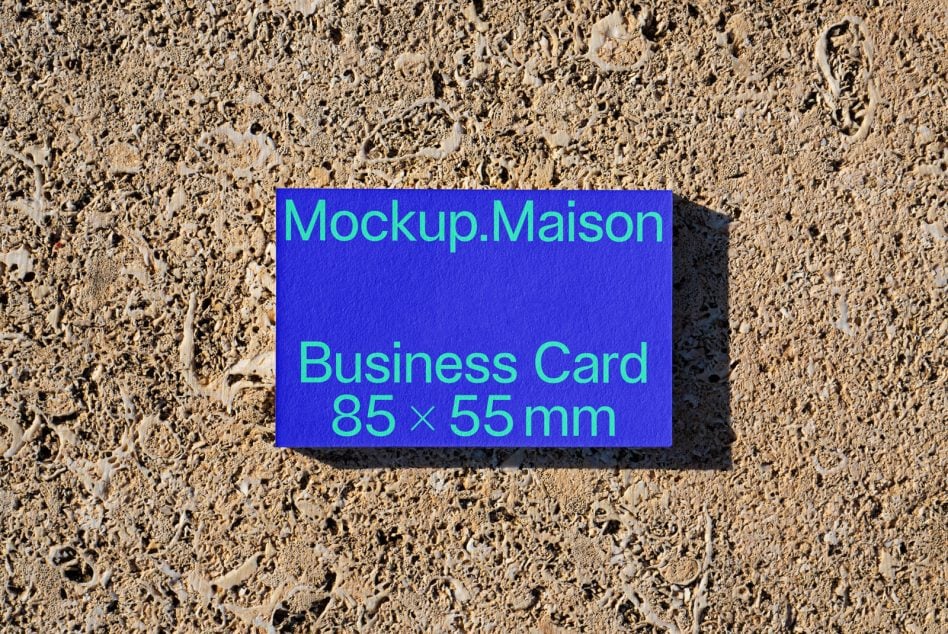 Blue business card with cyan type specs resting on rough cream-colored texture