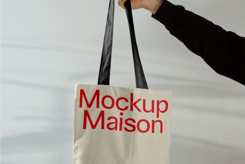 Person carrying natural canvas tote with black straps, red Mockup Maison text printed