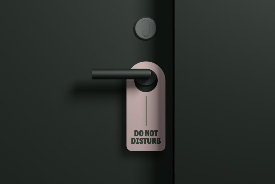 Pink do not disturb tag hanging from door handle on dark wall