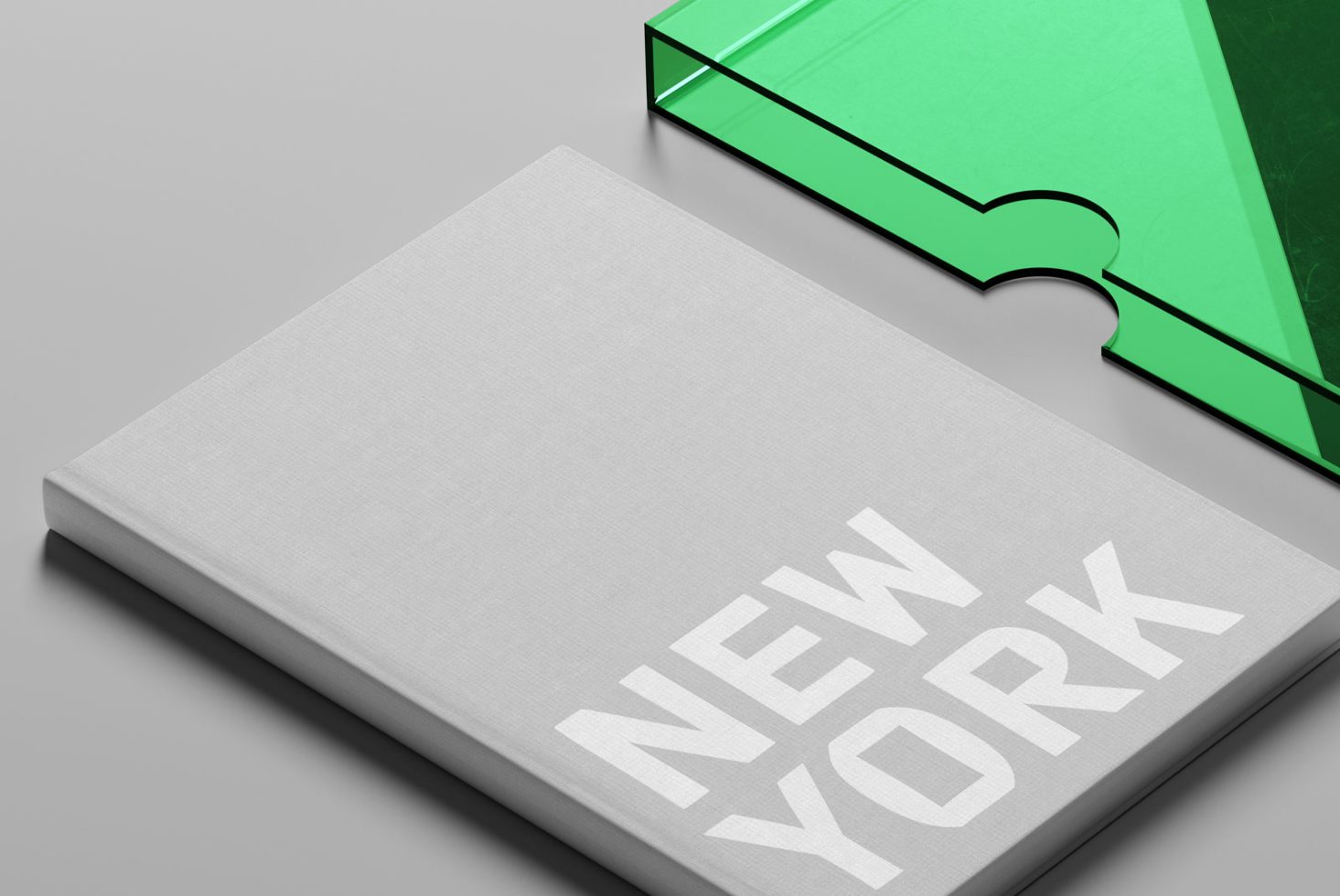 Hardcover book mockup with typographic design "NEW YORK" on cover, beside a green glass object, for design asset marketplace.