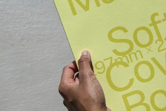 Person holding yellow paper with typography design, close-up on hand and print, graphic design, font showcase, paper texture.