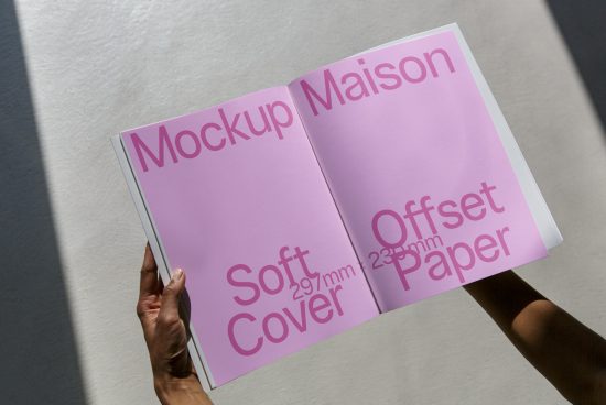 Person holding an open magazine mockup with pink cover, showcasing design and paper quality under natural light.