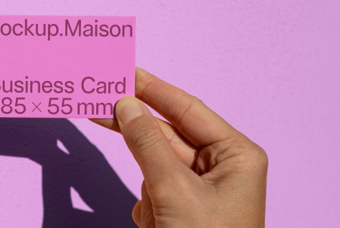 Hand holding a pink business card mockup with dimensions against a purple background, ideal for designers to showcase branding.