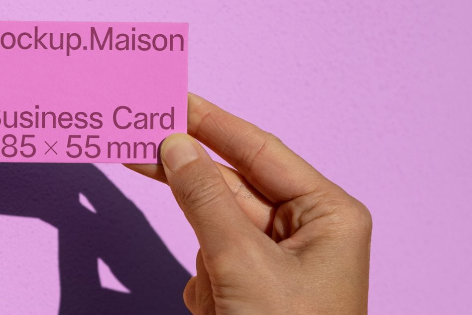 Fingers gripping pink business card with purple text on pink backdrop
