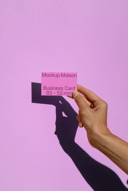 Hand holding pink business card against pink wall with shadow