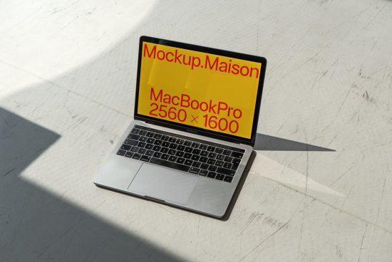 Laptop mockup on a white surface with sunlight casting shadows, displaying screen resolution, ideal for MacBook Pro template designs.