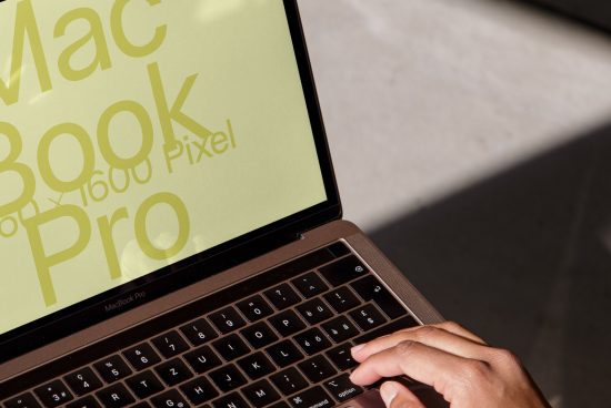 Close-up of a designer working on a MacBook Pro with stylized text mockup on screen, showcasing font and graphics in a modern template.