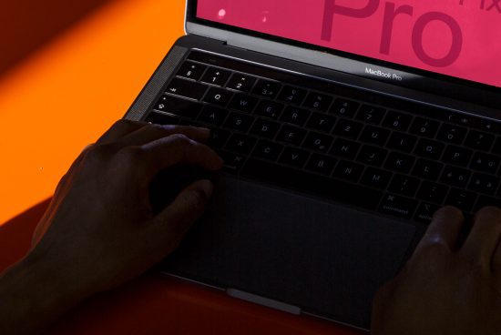 Close-up of designer's hands typing on MacBook Pro laptop with striking orange background, ideal for tech mockups, digital design assets.