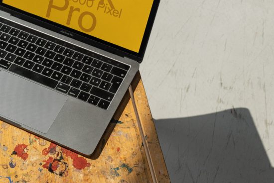 Laptop on a vintage wooden desk showcasing a graphic design on screen, with a sunlit modern workspace setting. Perfect for mockup graphics display.