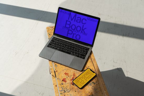 Laptop and smartphone mockup on a wooden table with a direct sunlight creating a shadow, perfect for design presentation in a realistic setting.