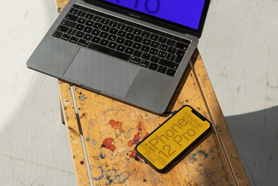 Laptop and smartphone on a paint-splattered table demonstrating a device mockup for design presentations, digital asset, creatives, UX/UI.