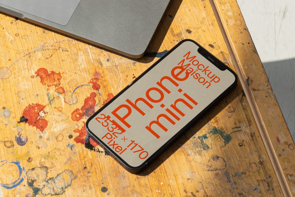 iPhone mini with red orange text on cream background sitting next to open laptop