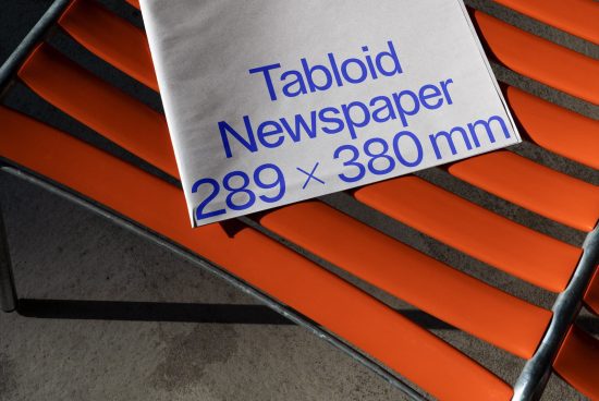 Printed tabloid newspaper mockup with dimensions on vibrant orange bench, showcasing realistic shadows and textures, ideal for media presentation.