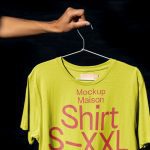 Hand holding hanger with lime green T-shirt mockup, graphic design display, dark backdrop, clothing template, apparel presentation.