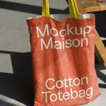 Red cotton tote bag mockup with yellow straps on a wooden easel, ideal for showcasing design work, relevant for graphics category.