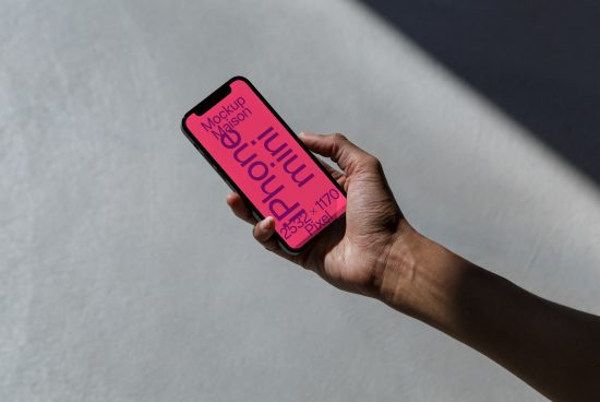 Hand holding smartphone with pink screen mockup for app design presentation, in natural light with shadow, digital assets for designers.