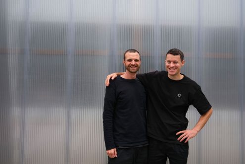 Two smiling men standing together in casual clothing with a corrugated metal background, ideal for mockup or template design.