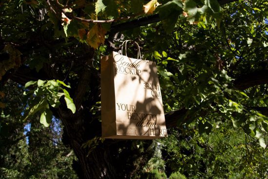 Eco-friendly paper bag mockup hanging on tree branch in natural outdoor setting, ideal for showcasing branding and packaging designs.