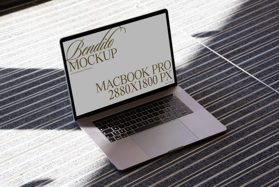 Laptop on striped carpet showcasing Bendito Mockup, MacBook Pro, digital device, realistic screen design, 2880x1800px, ideal for design presentation.