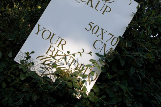 Poster mockup with gold typography overlay, nestled among green leaves, demonstrating natural outdoor presentation for designers.