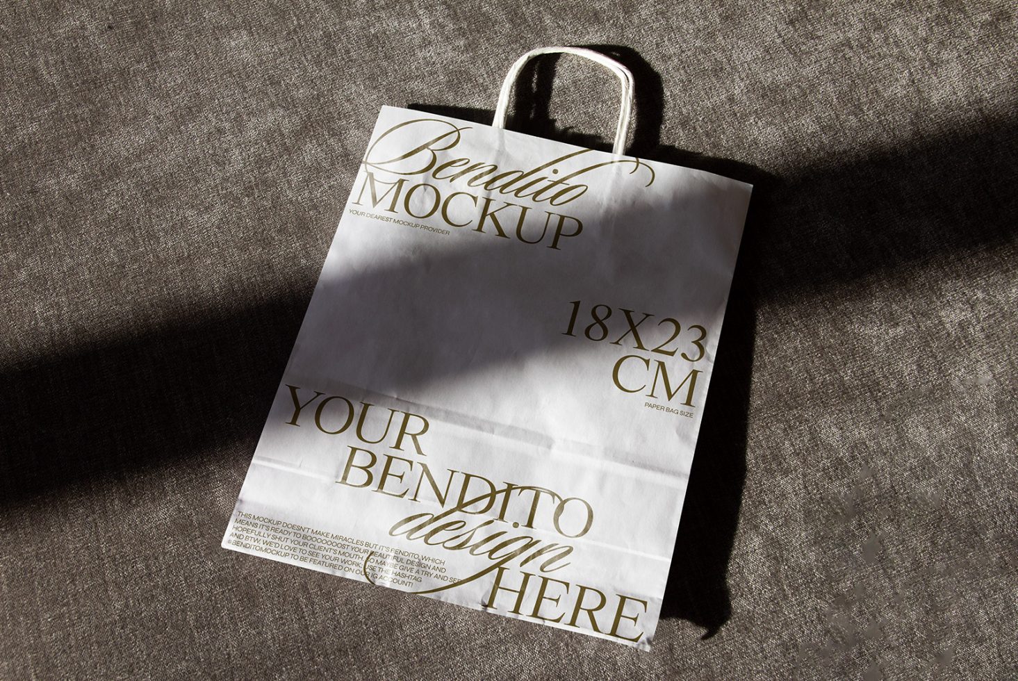 Elegant paper bag mockup lying on textured fabric under natural light, showcasing customizable design area for branding presentations.