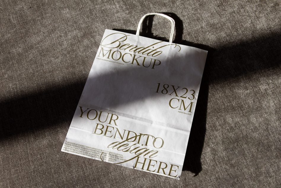 White paper bag with black handles on textured gray background with gold foil text