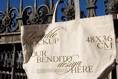 Canvas tote bag mockup hanging on a metal fence, natural lighting, design space available, perfect for showcasing custom graphics and fonts.