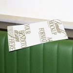 Mockup of a flyer with elegant typography leaning on a green leather sofa for design presentation.