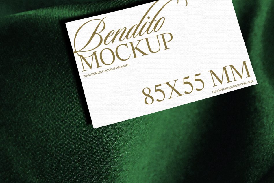 Elegant business card mockup on green fabric showcasing gold typography design, ideal for designers presentations 85x55mm European standard size.