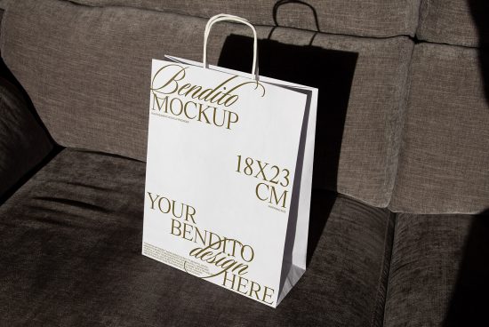 Elegant shopping bag mockup on sofa with customizable design area in gold font, ideal for presentations, digital assets for designers.