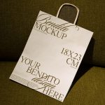 Elegant paper bag mockup on green fabric, showcasing design space with dimensions, perfect for presentations in Mockups category for designers.