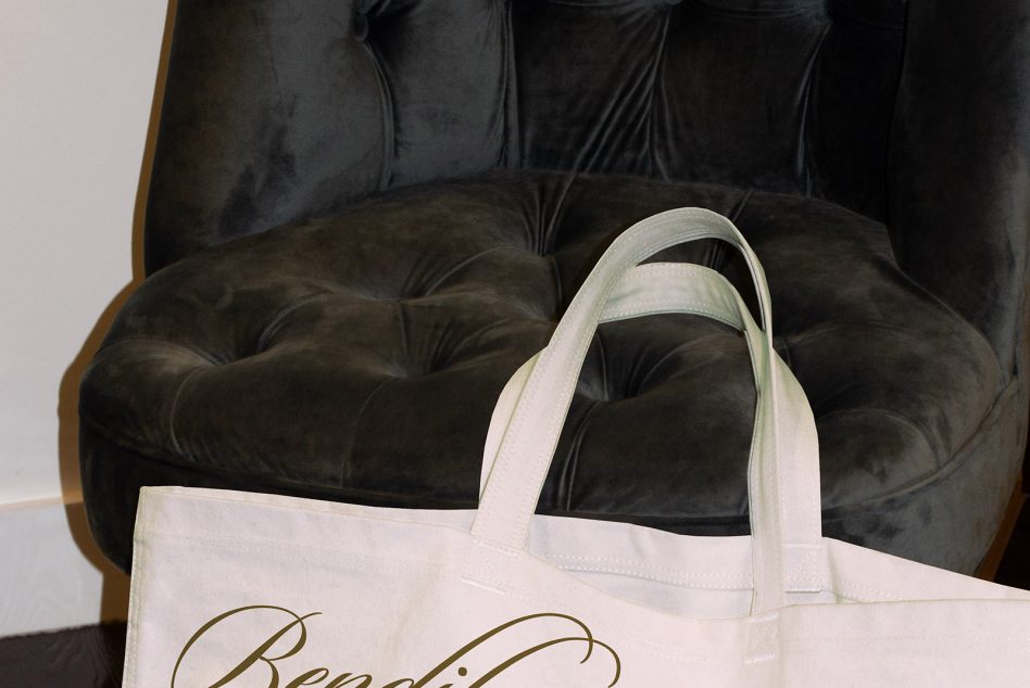 White tote bag resting on dark leather chair seat, minimal crop of handles