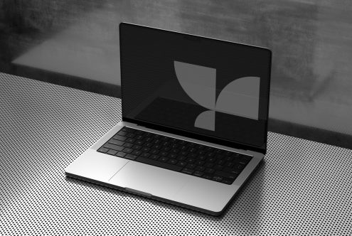 Silver laptop on gray textured surface with geometric shapes on black screen