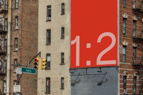 Urban billboard mockup with 1:2 ratio on a red background, juxtaposed against old buildings and a street sign, ideal for poster graphics.