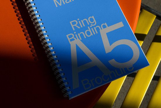 Blue A5 ring binding brochure mockup on orange surface with dramatic lighting, emphasizing print design and spiral binding for designers.