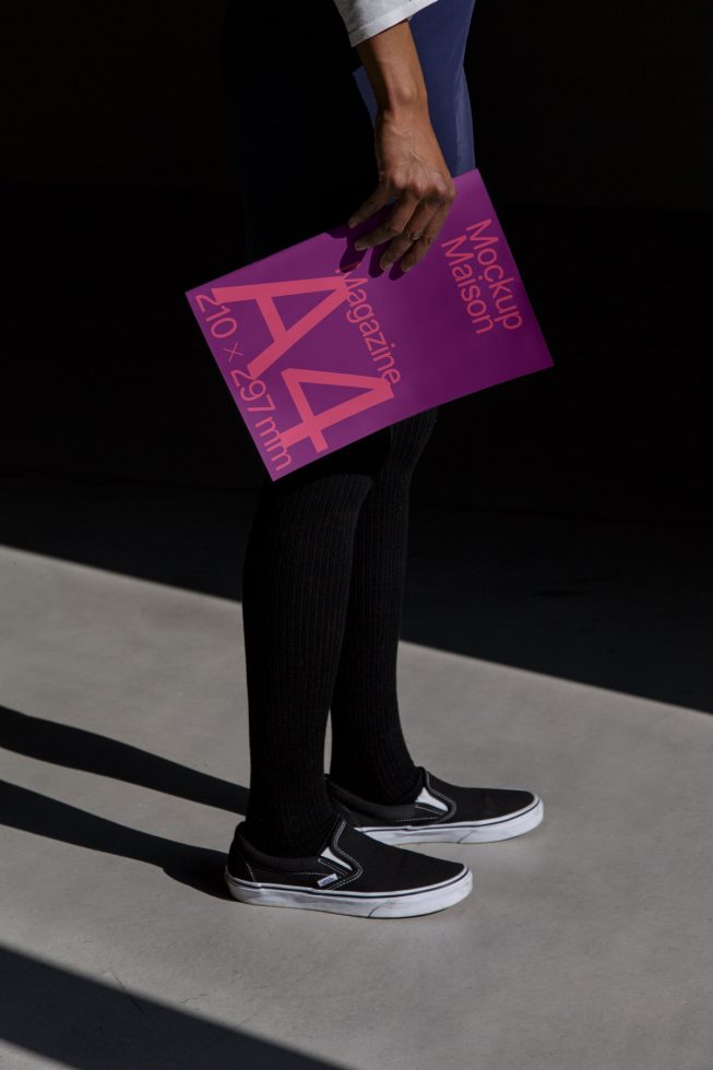 Person holding a purple magazine mockup in sunlight, showcasing design and layout potential for print templates, ideal for graphic designers.