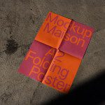 A2 size folded poster mockup in orange and pink with typography, resting on a textured concrete floor in sunlight for design presentation.