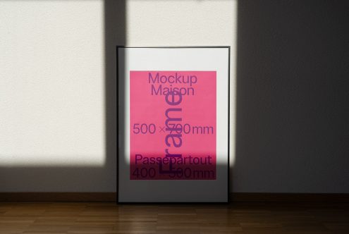 Modern poster frame mockup standing on wooden floor against white wall with shadows, realistic template for designers.