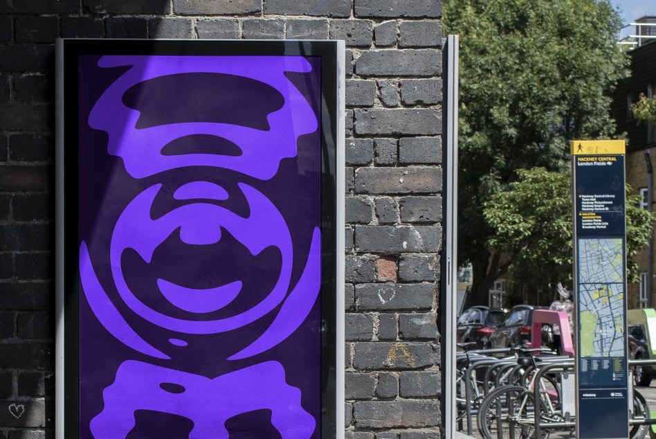 Street-mounted display with stacked purple character designs in bright neon