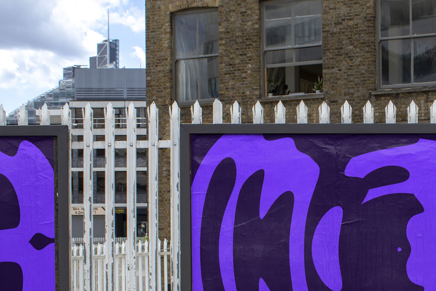 Urban street art on wall with purple graffiti, white picket fence, and brick building backdrop for design inspiration in mockups and templates.