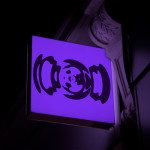 Illuminated purple signboard mockup with abstract design hanging on a dark wall, ideal for storefront branding graphics.