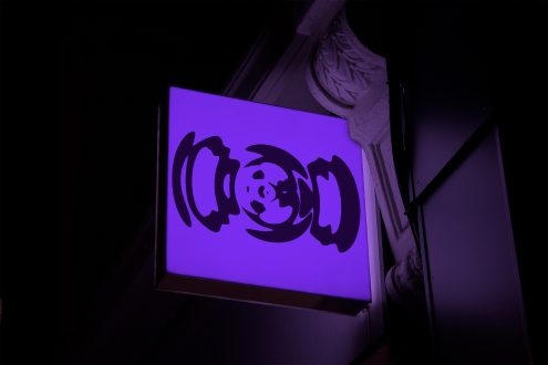 Illuminated purple signboard mockup with abstract design hanging on a dark wall, ideal for storefront branding graphics.