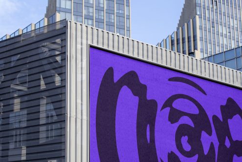 Billboard mockup with purple abstract design in urban setting, clear skies, ideal for outdoor advertising graphics presentation.