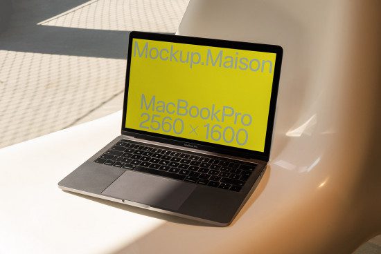 Laptop mockup on white table against beige backdrop displaying bright yellow screen with text digital designers asset MacBook Pro.
