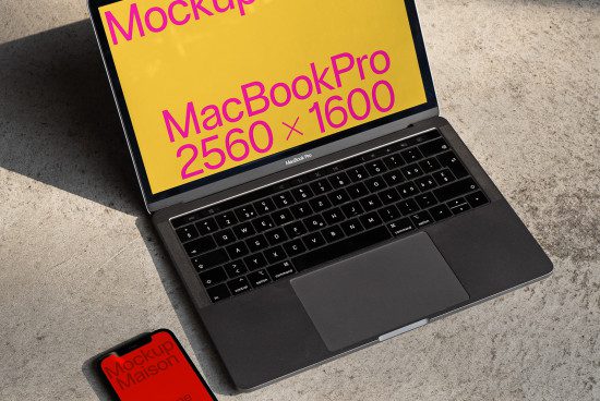 Laptop mockup with screen displaying resolution, placed on concrete surface next to smartphone with branding logo, ideal for presentations.