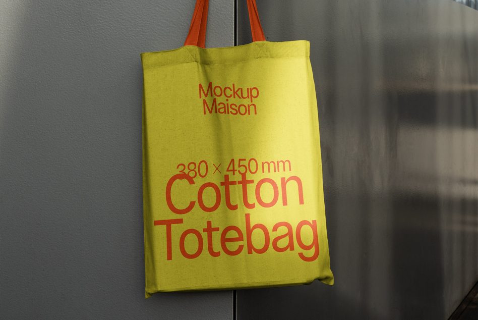 Green cotton tote bag mockup with red text hanging on a wall, realistic design asset for branding and packaging.