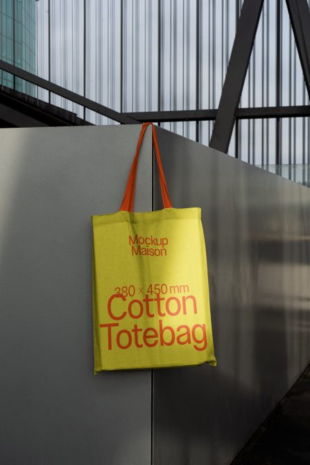 Yellow tote bag mockup hanging against urban backdrop with clear space for branding, perfect for designers showcasing graphics and prints.